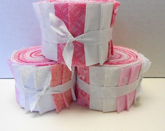 May include: Three rolls of pink and white fabric scraps tied with white ribbon. The fabric has a variety of patterns, including floral and geometric designs.