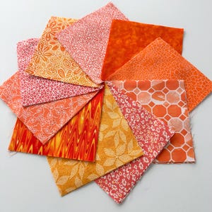 May include: A collection of orange and red fabric squares arranged in a circular pattern. The fabrics feature various patterns, including floral, swirls, and geometric designs. The color palette ranges from light orange to deep red.