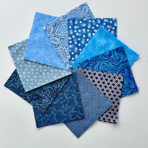May include: A collection of blue fabric squares arranged in a circular pattern. The squares feature various patterns, including paisley, floral, and abstract designs. The shades of blue range from light to dark, creating a visually appealing display of textiles.