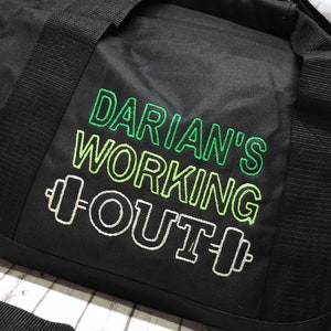 May include: Black duffel bag with a green and white embroidered design that says "Darian's Working Out" with a dumbbell on each side of the word "Out".