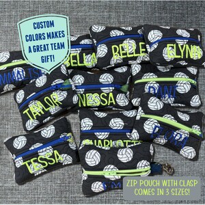 May include: A collection of black and white volleyball-patterned zipper pouches with various names embroidered in green and blue. The pouches come in three sizes and have a clasp.