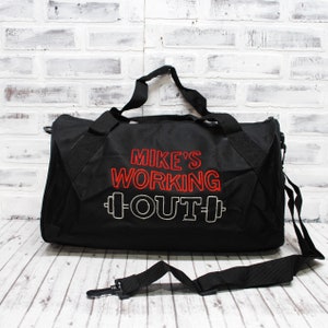 May include: Black duffel bag with a red embroidered design that says "Mike's Working Out" with a dumbbell graphic on either side of the word "Out".