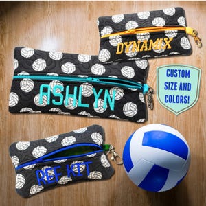 May include: Three black zippered pouches with a volleyball pattern. The pouches are personalized with the names "Dynamix", "Ashlyn", and "Ref Kit". A blue volleyball is in the foreground.