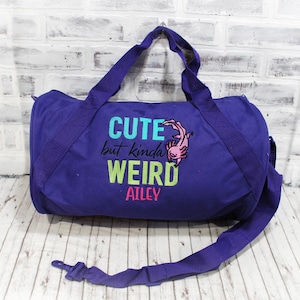 May include: Purple duffel bag with a pink axolotl graphic and the text "Cute but kinda weird Ailey".