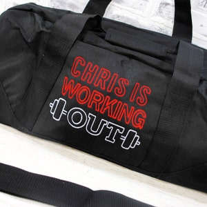 May include: Black duffel bag with a red and white embroidered design that says "Chris is working out" with a dumbbell graphic on either side of the text.