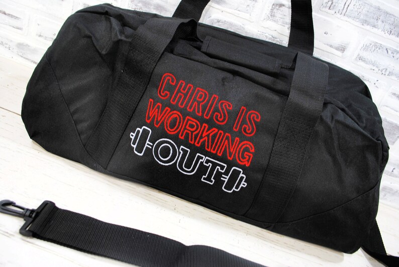 May include: Black duffel bag with a red and white embroidered design that says "Chris is working out" with a dumbbell graphic on either side of the text.