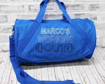 May include: A vibrant blue duffel bag with a shoulder strap and handles. The bag features the text "MARCO'S WORKING OUT" in white and black, with a barbell graphic. The bag is designed for gym or sports use.