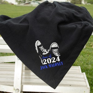 Peut inclure: Une couverture en polaire noire avec un graphique blanc de deux baskets et le texte "class of 2024 JACK MALONEY" en blanc avec "class of" en bleu.