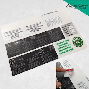 Op de afbeelding: Een set zwarte en witte stickers met instructies en waarschuwingen voor een voertuig. De stickers bevatten tekst in het Engels, Frans, Duits en Spaans. De stickers zijn op een witte achtergrond. Er is ook een groen-witte sticker met de tekst "RON 98 AANBEVOLEN".