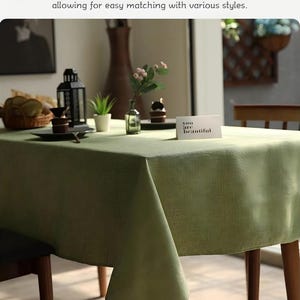 Puede incluir: Un mantel verde salvia con apariencia texturizada, sobre una mesa de madera. El texto "High gram weight, natural drape" es visible. La mesa está decorada con elementos decorativos, incluyendo una pequeña planta y una tarjeta que dice "you are beautiful."
