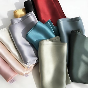 May include: A collection of folded silk fabric in various colors, including red, black, teal, gray, and cream. The fabric has a smooth, shiny texture, and the folds create shadows and highlights.