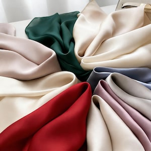 May include: A collection of silk scarves in various colors, including red, cream, green, and blue. The scarves are arranged in a circular pattern, showcasing their smooth texture and vibrant hues. The image highlights the luxurious feel of the fabric.