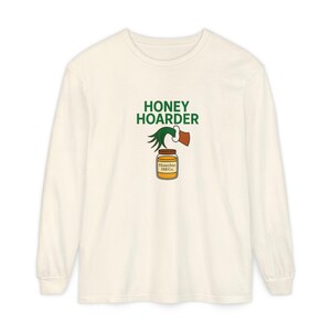 May include: Cream-colored long-sleeve shirt with the words "HONEY HOARDER" in green above a graphic of a honey jar with a bee and a honey dipper. The honey jar has the text "Honeybee Hill Co." on it.