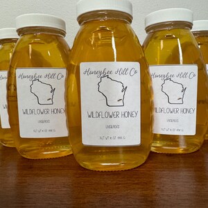 May include: Eight glass jars of unfiltered wildflower honey, each labeled "Honeybee Hill Co. Wildflower Honey Ungraded Net Wt 12 oz (340 g)" with a black and white illustration of the state of Wisconsin.