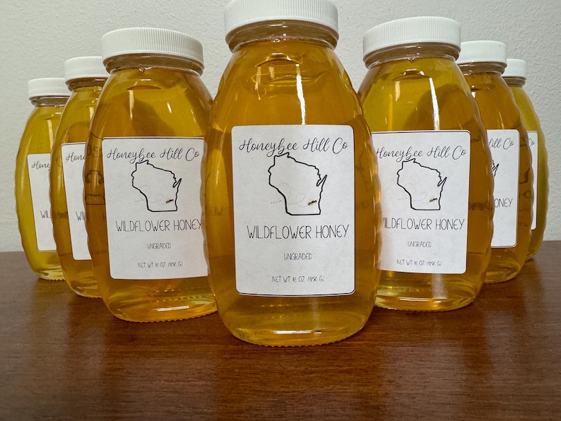 May include: Eight glass jars of unfiltered wildflower honey, each labeled "Honeybee Hill Co. Wildflower Honey Ungraded Net Wt 12 oz (340 g)" with a black and white illustration of the state of Wisconsin.