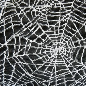 May include: Close-up of a black and white woven fabric. The design features a repeating pattern of white lines forming a web-like structure against a black background. The texture appears to be slightly raised.