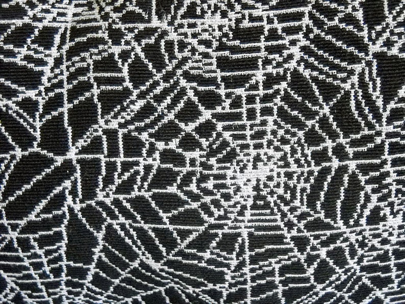 May include: Close-up of a black and white woven fabric. The design features a repeating pattern of white lines forming a web-like structure against a black background. The texture appears to be slightly raised.