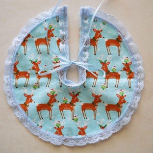 Può includere: Una gonna per albero di Natale azzurra con un motivo ripetuto di renne marroni con accessori festivi. La gonna è rifinita con pizzo azzurro e legata con un nastro abbinato. Una decorazione festiva stagionale.