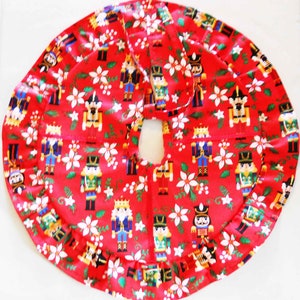 May include: A red Christmas tree skirt with a repeating pattern of nutcrackers and white poinsettias. The skirt has a ruffled edge and a center opening for the tree trunk. The festive design is perfect for holiday decor.