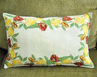 May include: A white pillow with a floral design featuring yellow lemons, red and orange flowers, and green leaves. The pillow is made of a soft, woven fabric.