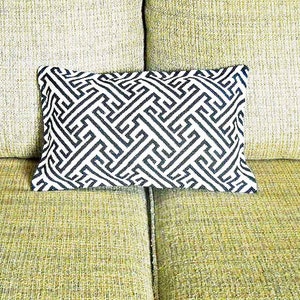 May include: A black and white geometric patterned throw pillow on a green couch.
