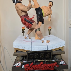 May include: A detailed statue depicting a martial arts fight scene. Two figures are engaged in combat, one executing a high kick. The statue features vibrant colors, including red, black, and gold, and is set on a platform with decorative elements.
