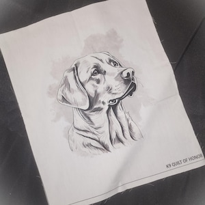 May include: A black and white illustration of a dog's head and shoulders, printed on a white fabric. The dog is looking up, with detailed shading. The text "K9 QUILT OF HONOR" is printed in black at the bottom right corner.