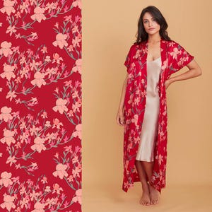 May include: A red floral print robe with short sleeves and a matching floral pattern on the left. The robe is worn over a light-coloured slip dress. The floral pattern includes pink flowers and green stems.