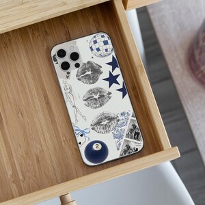 May include: A white phone case with a collage design featuring a disco ball, navy blue stars, and three sets of gray lipstick prints. Additional elements include a fashion sketch, a blue billiard ball with the number 2, and a blue and white patterned design.