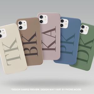 Peut inclure: Cinq coques de téléphone de couleurs variées : beige, marron, mauve, bleu et vert. Chaque coque présente une grande initiale ou des initiales en une teinte plus foncée que la couleur de la coque. Les coques sont présentées sur un fond gris clair.