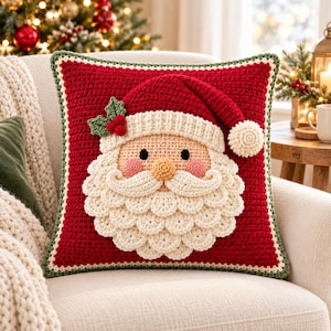 May include: A square crochet throw pillow featuring a red background with a central Santa Claus face design. The Santa has a cream-colored beard, a red hat with a white pom-pom, pink cheeks, and a green holly sprig with red berries on the side.