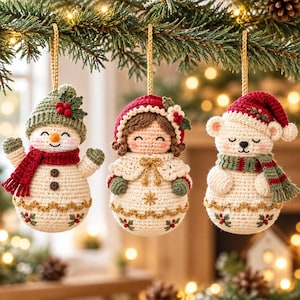 Può includere: Tre ornamenti all'uncinetto appesi a fili dorati. A sinistra un pupazzo di neve con cappello verde e sciarpa rossa. Al centro una bambola con cuffia rossa e mantella bianca. A destra un orso bianco con cappello rosso e sciarpa a righe.