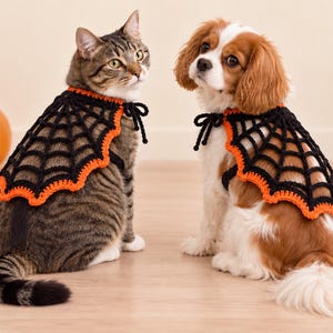 May include: Two crocheted pet capes featuring a black spiderweb pattern with a vibrant orange scalloped border. Each cape includes black ties at the neck for fastening. The design is crafted with a detailed web motif and a contrasting edge.