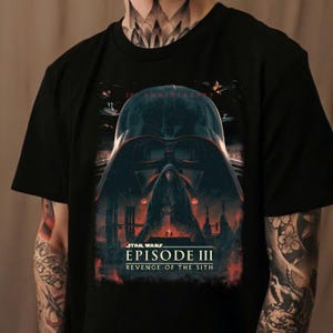Può includere: Maglietta nera con una grafica di Darth Vader di Star Wars Episodio III: La vendetta dei Sith. La grafica è in rosso, bianco e nero.