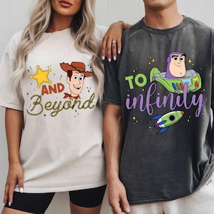 Puede incluir: Dos camisetas con gráficos de Toy Story. Una es beige con Woody y el texto "And Beyond". La otra es gris oscuro con Buzz Lightyear y el texto "To Infinity". Ambas camisetas tienen un corte holgado.