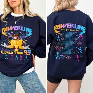 May include: Navy blue sweatshirt with a colorful graphic featuring the text "PAWERLINE" and "Stand Out World Tour 95". The design includes a cartoon character and tour locations. The back of the sweatshirt lists tour cities.