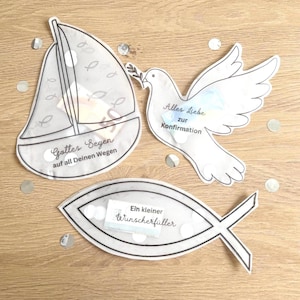 Könnte beinhalten: Drei weiße Papierausstanzungen auf einer Holzoberfläche. Die Ausstanzungen umfassen ein Segelboot mit dem Text "Gottes Segen auf all Deinen Wegen", eine Taube mit dem Text "Alles Liebe zur Konfirmation" und einen Fisch mit dem Text "Ein kleiner Wunscherfüller".
