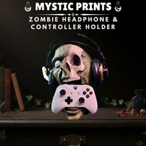 May include: A zombie skull headphone and controller holder. The skull is green and tan, with headphones resting on its head and a white Xbox controller in its mouth. The text "MYSTIC PRINTS" and "ZOMBIE HEADPHONE & CONTROLLER HOLDER" are at the top.