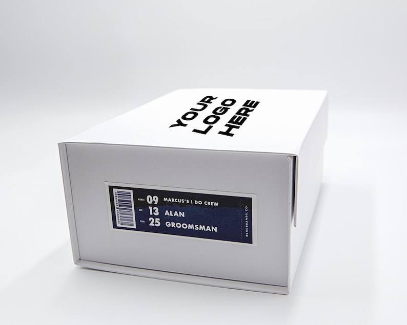 May include: A white box with the text "YOUR LOGO HERE" printed on the top. A label on the side reads "MARCUS'S I DO CREW", with the names "ALAN" and "GROOMSMAN" listed below. The box is on a white surface.