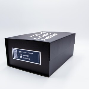 May include: A black box with the text "YOUR LOGO HERE" in white on the top. A label on the side includes a barcode and the text "-09 MARCUS' I DO CREW -13 JACOBY -25 BEST MAN".