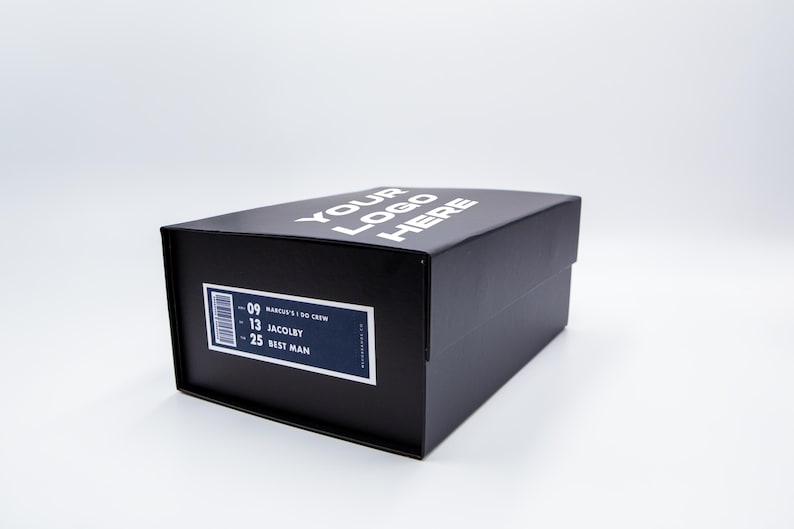 May include: A black box with the text "YOUR LOGO HERE" in white on the top. A label on the side includes a barcode and the text "-09 MARCUS' I DO CREW -13 JACOBY -25 BEST MAN".