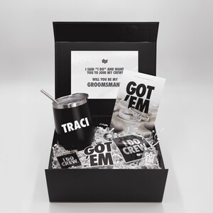 May include: A black gift box containing a black tumbler with "TRACI" in white, a card that says "GOT 'EM", and several stickers. The box also contains a card that says "I SAID 'I DO' AND WANT YOU TO JOIN MY CREW! WILL YOU BE MY GROOMSMAN".