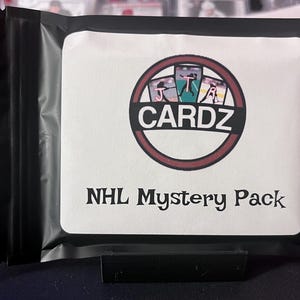 May include: A black and white bag with a white label that says "NHL Mystery Pack" and a red circle with the word "CARDZ" in white letters. The circle has a picture of hockey cards inside.