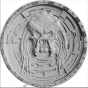 May include: A silver coin with a detailed, three-dimensional image of a Predator's head. The Predator's face is fierce, with sharp teeth and a menacing expression. The coin is surrounded by a circular pattern of intricate designs.