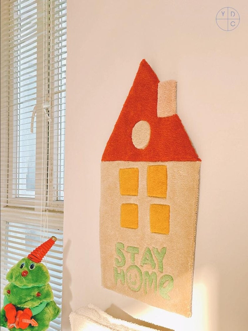 May include: A beige and orange felt house-shaped wall hanging with the words "STAY HOME" in green felt.