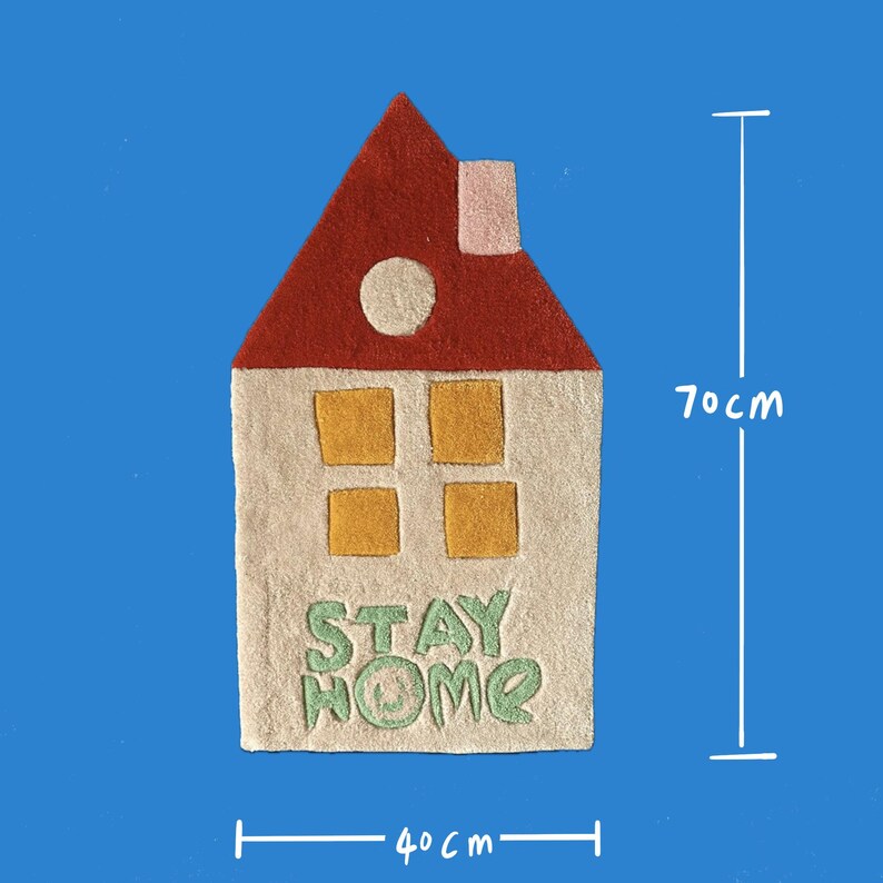 May include: A white felt house rug with a red roof, four yellow windows, and the words "STAY HOME" in green. The rug measures 40 inches wide and 70 inches tall.