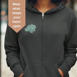 Unisex dark gray zip hoodie with heart chakra mandala design, photographed outdoors. Spiritual clothing inspired by openness, emotional balance and self-connection, perfect for mindful everyday wear.
