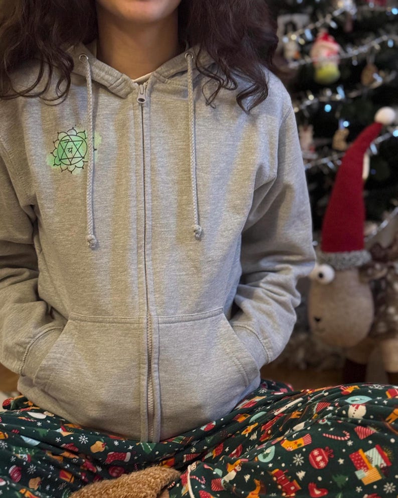 Front view of grey zip hoodie with small green chakra symbol on chest, relaxed cozy home look