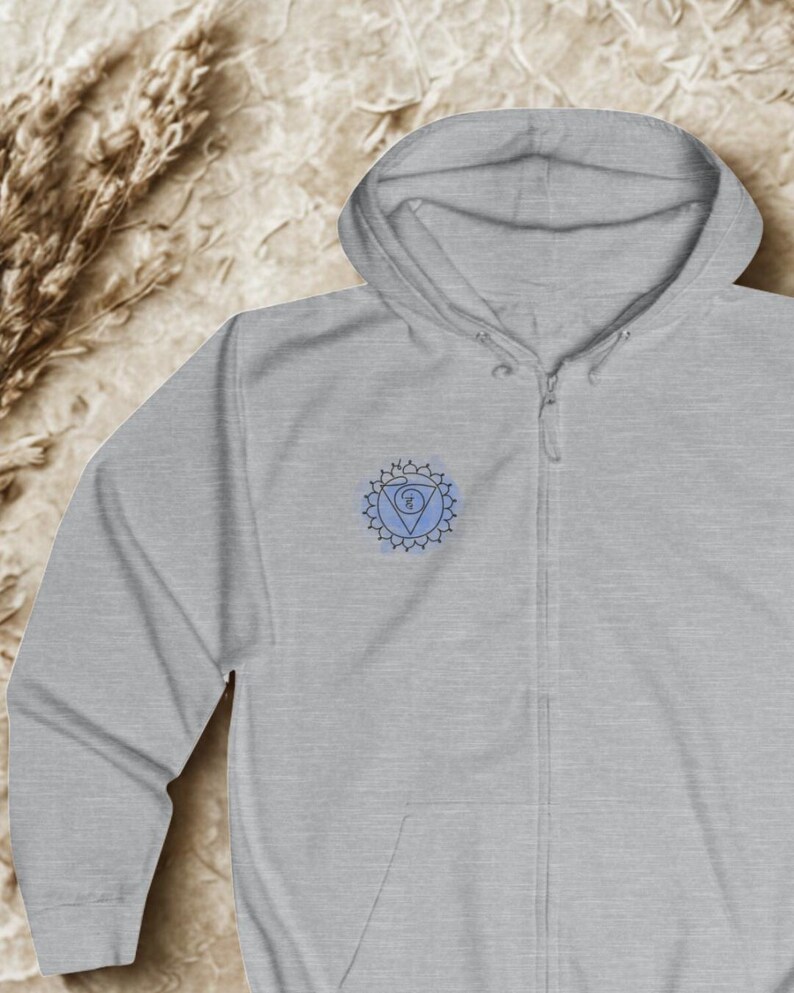 Light gray unisex zip hoodie featuring blue chakra mandala on the chest. Minimal spiritual hoodie presented in flat lay composition, designed for mindful everyday wear and inner balance.