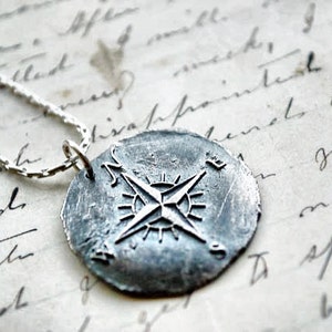 Könnte beinhalten: Eine silberne Kompass-Anhänger-Halskette mit einem detaillierten Kompass-Design. Der Kompass befindet sich an einer silbernen Kette.